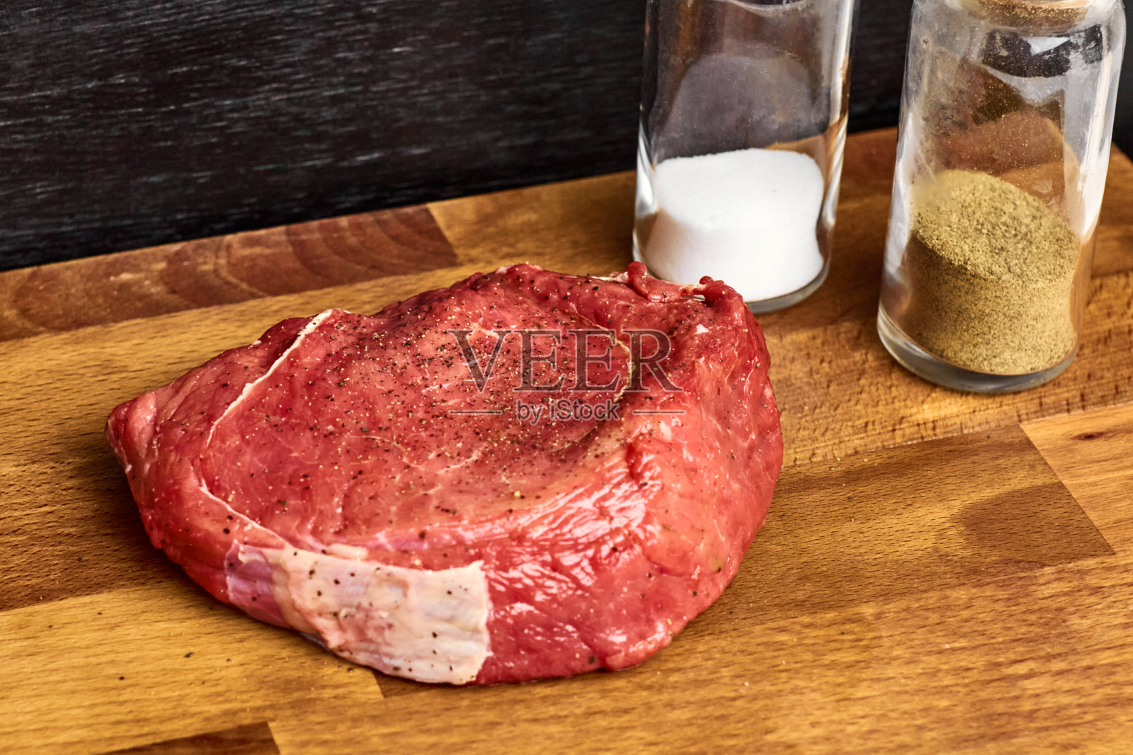 一块新鲜的牛肉,旁边放着盐瓶和胡椒瓶,放在木板上。收据的概念。照片摄影图片