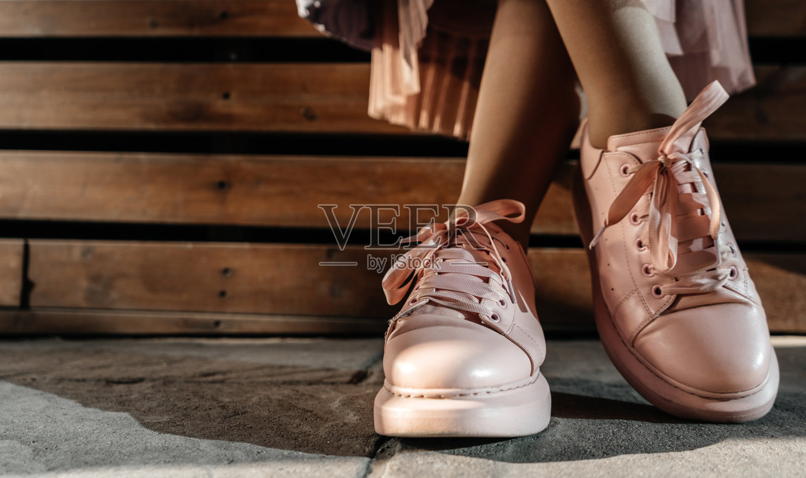 年轻时尚女人的腿在休闲粉色鞋。鞋。木制背景上的粉色运动鞋照片摄影图片