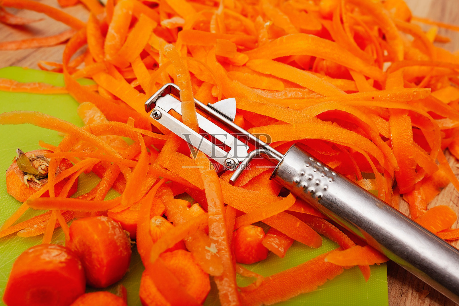 用不锈钢蔬菜削皮器将新鲜的胡萝卜磨碎,切成串放在绿色砧板上照片摄影图片