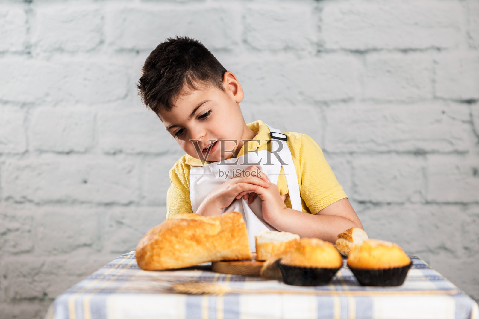 一个男孩打扮成面包师,在他的面包、面粉和松饼的面包店里开心地笑着。照片摄影图片