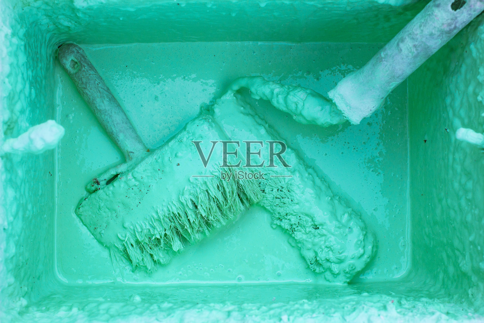 油漆滚筒和刷子在桶中与乳剂在混凝土摊铺,前面和背景模糊与散景效果照片摄影图片