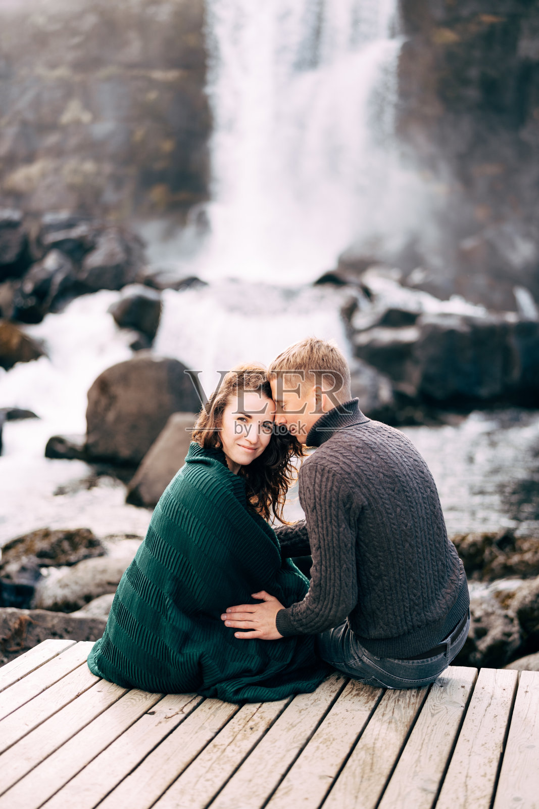 一个男孩和一个女孩坐在埃萨罗河瀑布附近的一座桥上拥抱。照片摄影图片
