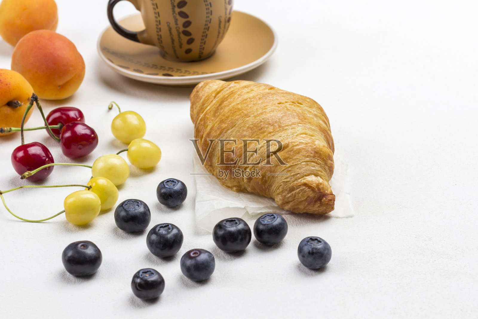 牛角面包,一杯咖啡,桌上有樱桃和蓝莓。照片摄影图片