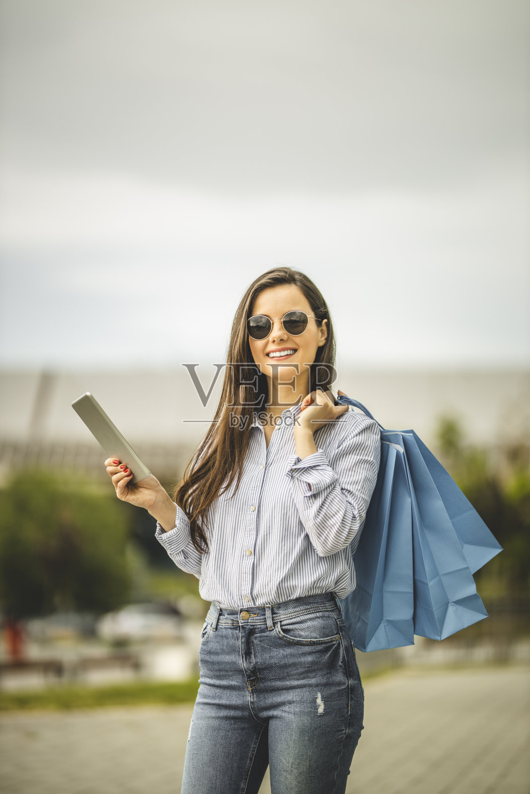 年轻漂亮的女人提着购物袋,用着平板电脑,走路照片摄影图片