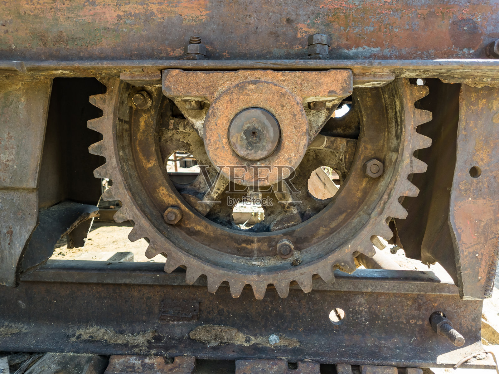 大型金属起重机齿轮,建筑设备上的锈蚀铁在一个夏天的日子里与轨道上的螺栓和螺母的特写。照片摄影图片