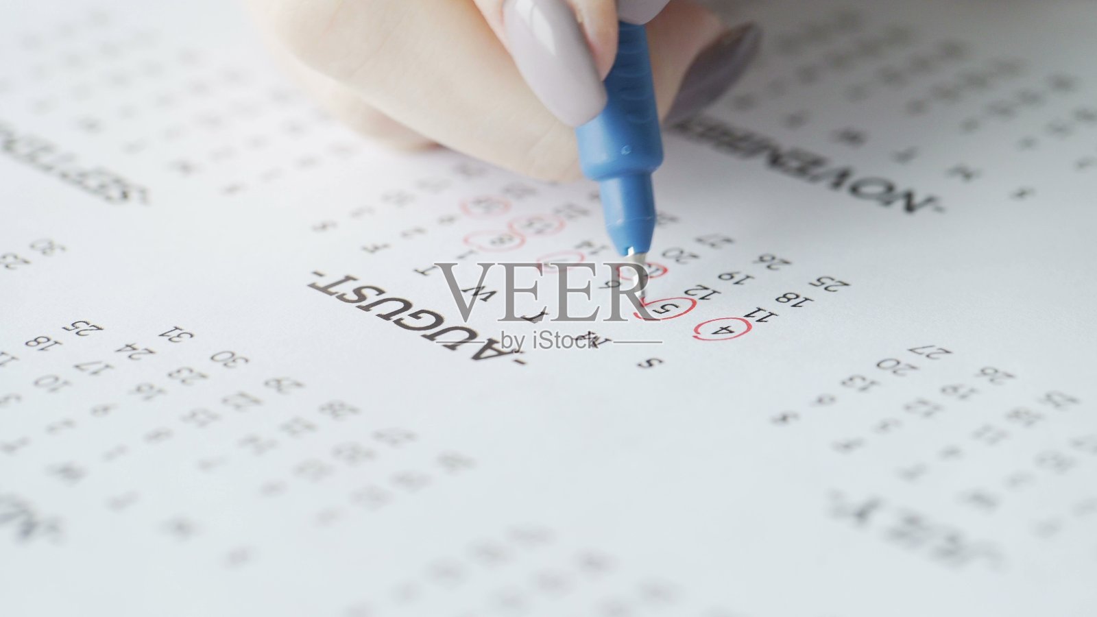 在纸日历上,妇女用手圈出八月四、五月天。照片摄影图片