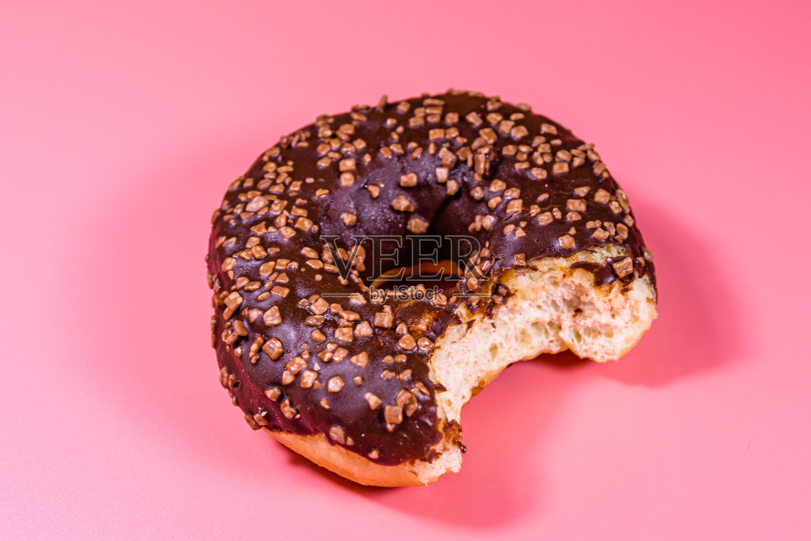被咬过的甜甜圈上涂着巧克力釉,孤立在粉红色的背景上照片摄影图片