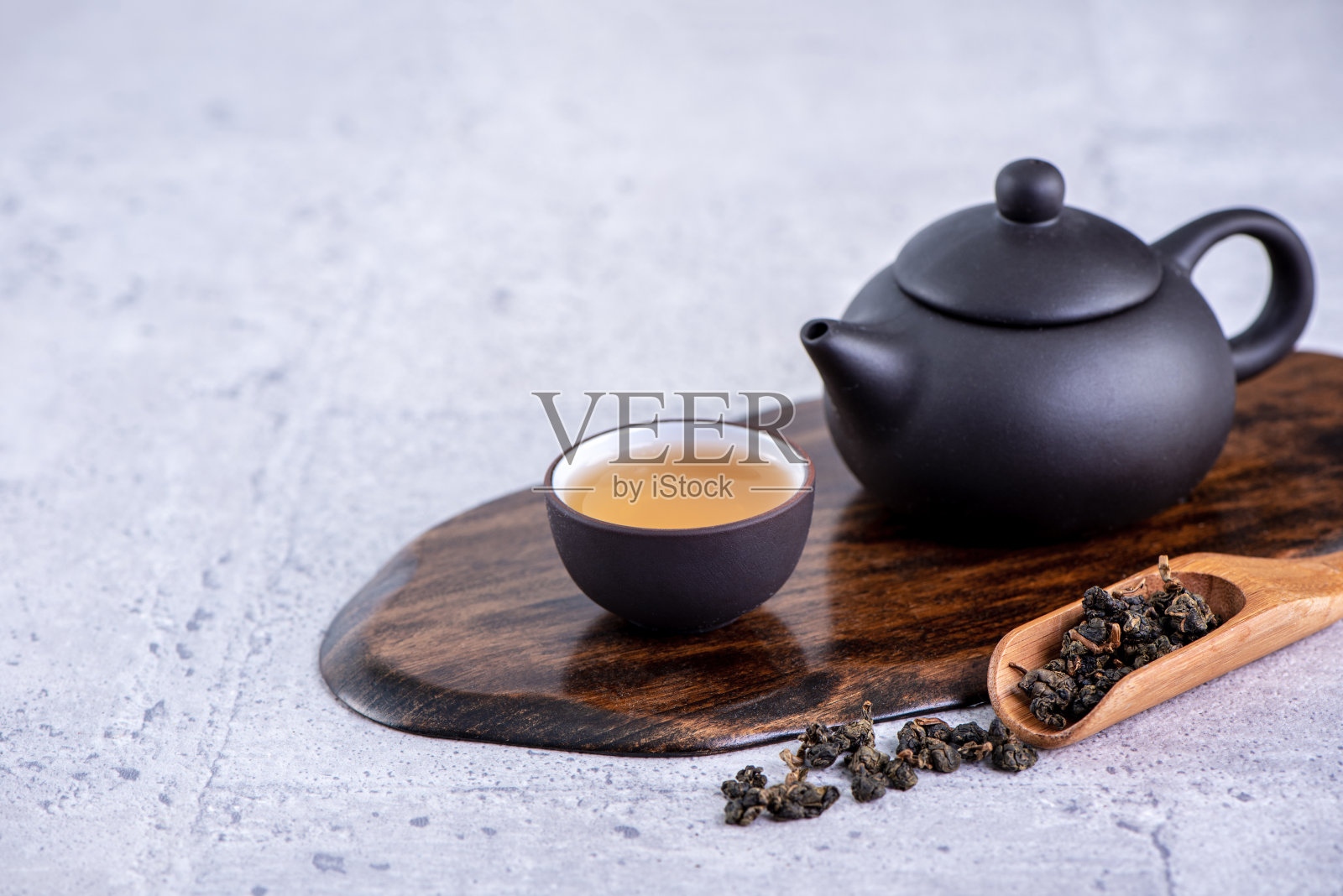 黑色茶壶和茶杯中的热茶,亮灰色水泥背景上的干茶叶,近距离复制空间的设计理念。照片摄影图片