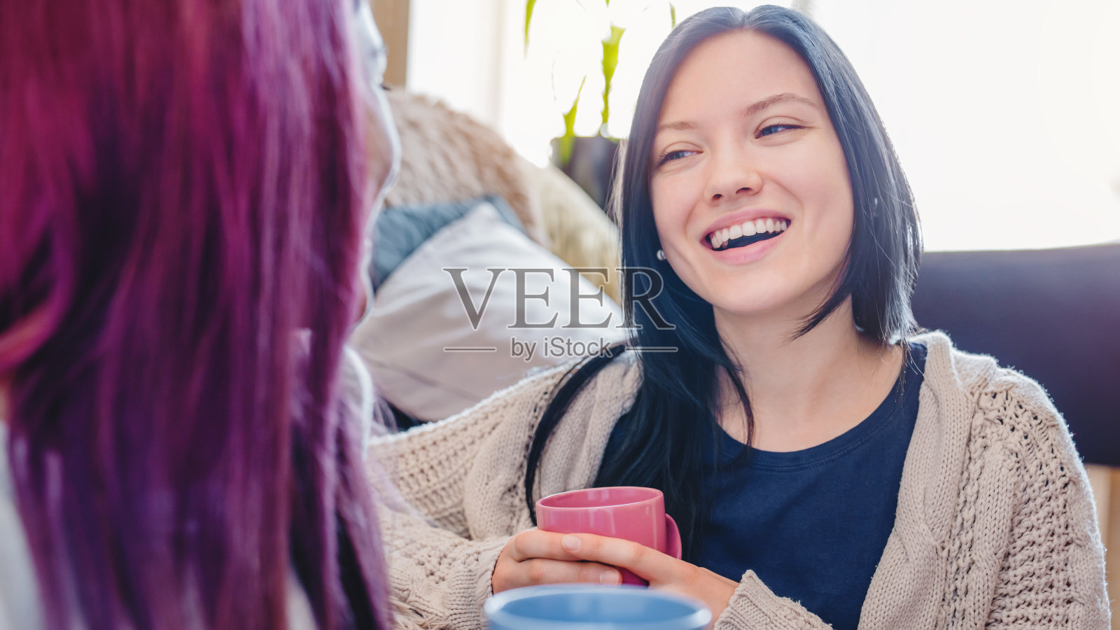 两个快乐的年轻白种女性朋友与咖啡杯交谈在客厅的家照片摄影图片