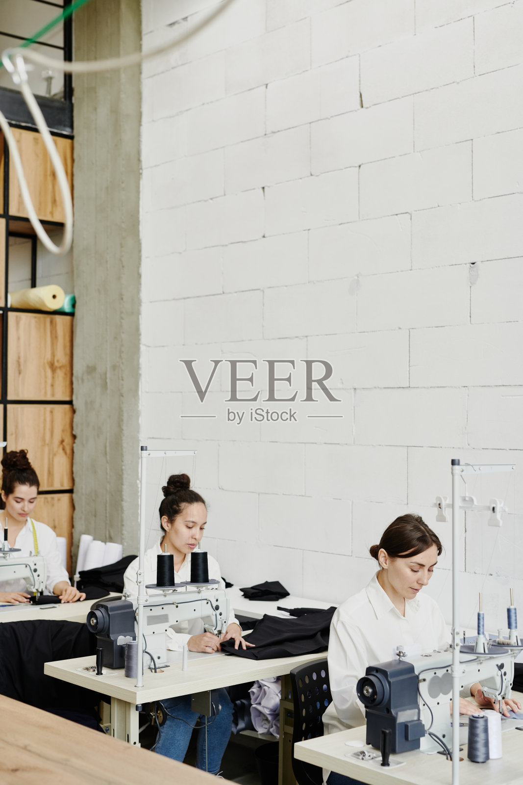 一排年轻的时装设计师坐在书桌旁,旁边放着电动缝纫机照片摄影图片