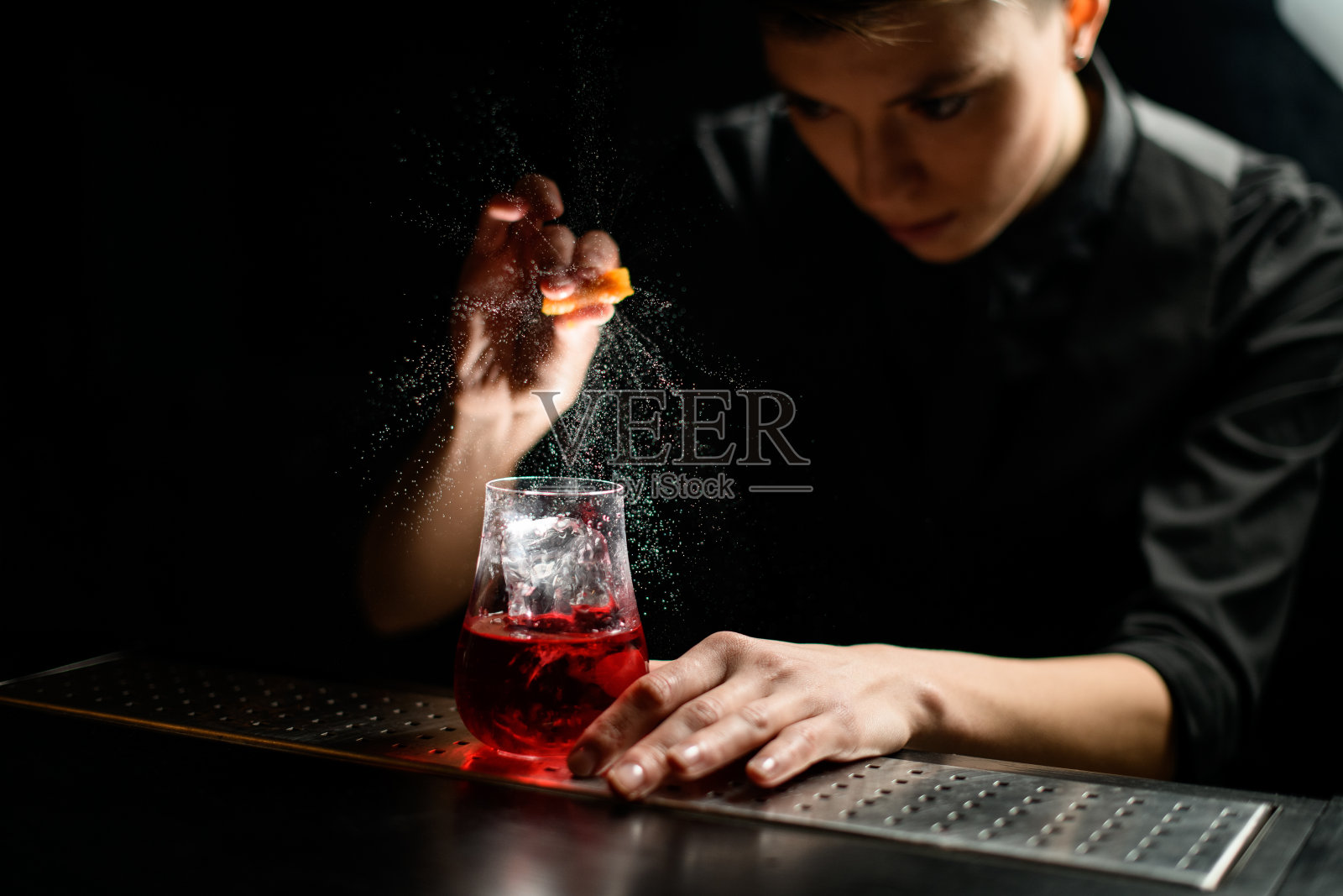 近距离的酒保轻轻地将红色鸡尾酒和冰块洒在玻璃杯上照片摄影图片