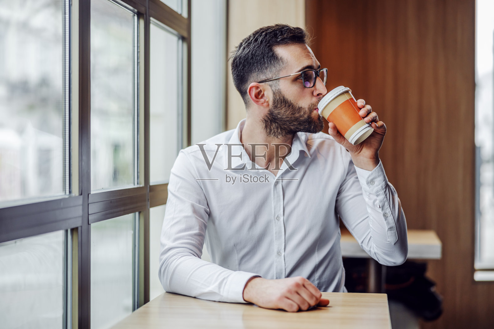 年轻英俊的胡子优雅的男子坐在自助餐厅喝新鲜的早晨用一次性杯子。照片摄影图片