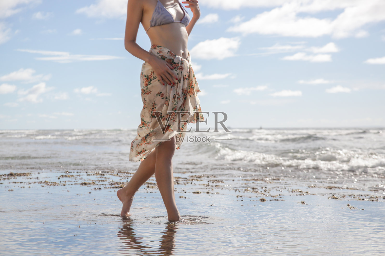 女人裹着花纱笼赤脚走在海滩上。照片摄影图片