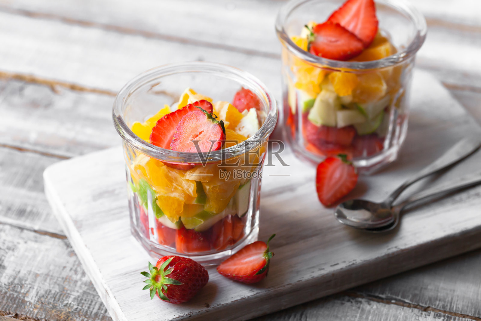 健康食品理念,清洁饮食。低卡路里的彩色甜夏日甜点。自制简单的水果沙拉,理想的早餐。橙、苹果、草莓。白色木质背景的文本复制空间照片摄影图片