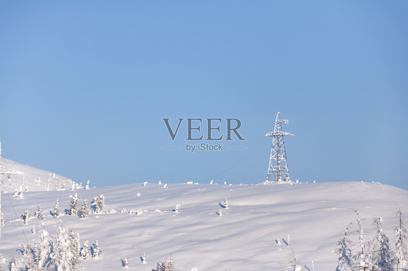 在晴朗的冬日里,湛蓝的天空下,高压输电塔和线路被皑皑白雪覆盖照片摄影图片