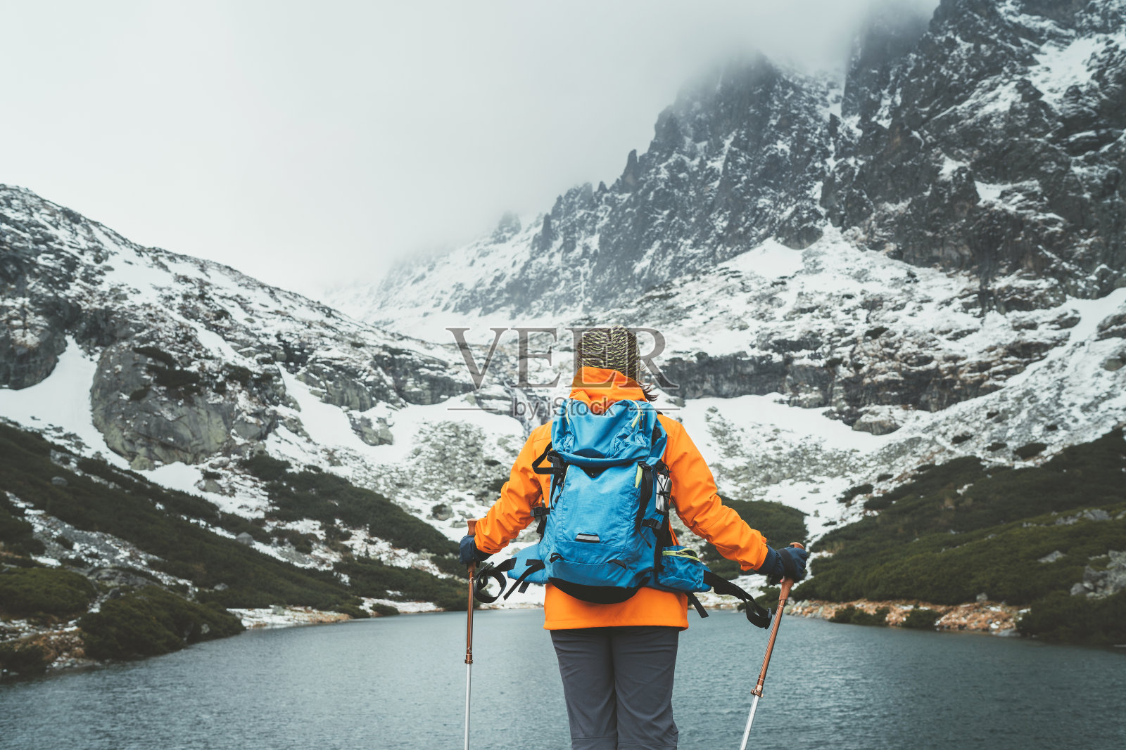 在斯洛伐克高地塔特拉斯的Velicka山谷徒步时,穿着亮橙色夹克的女性背包客拿着登山杖,欣赏Velicke pleso(山湖)风景。活跃的人的概念照片摄影图片