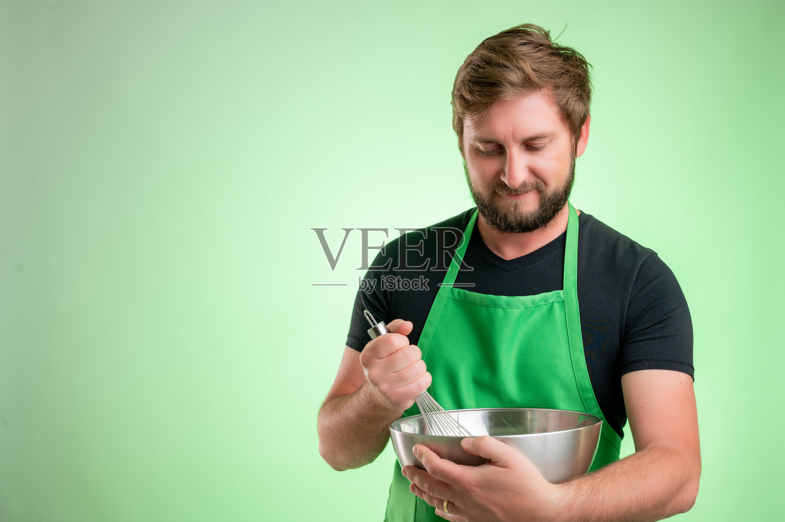 一名穿着黑色t恤,系着绿色围裙的超市员工,手里拿着金属碗和铁丝照片摄影图片