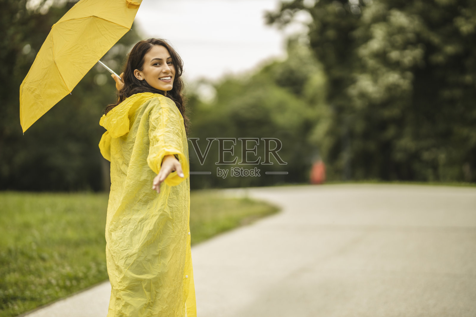 拿着黄伞,穿着黄雨衣,享受着雨的女人照片摄影图片