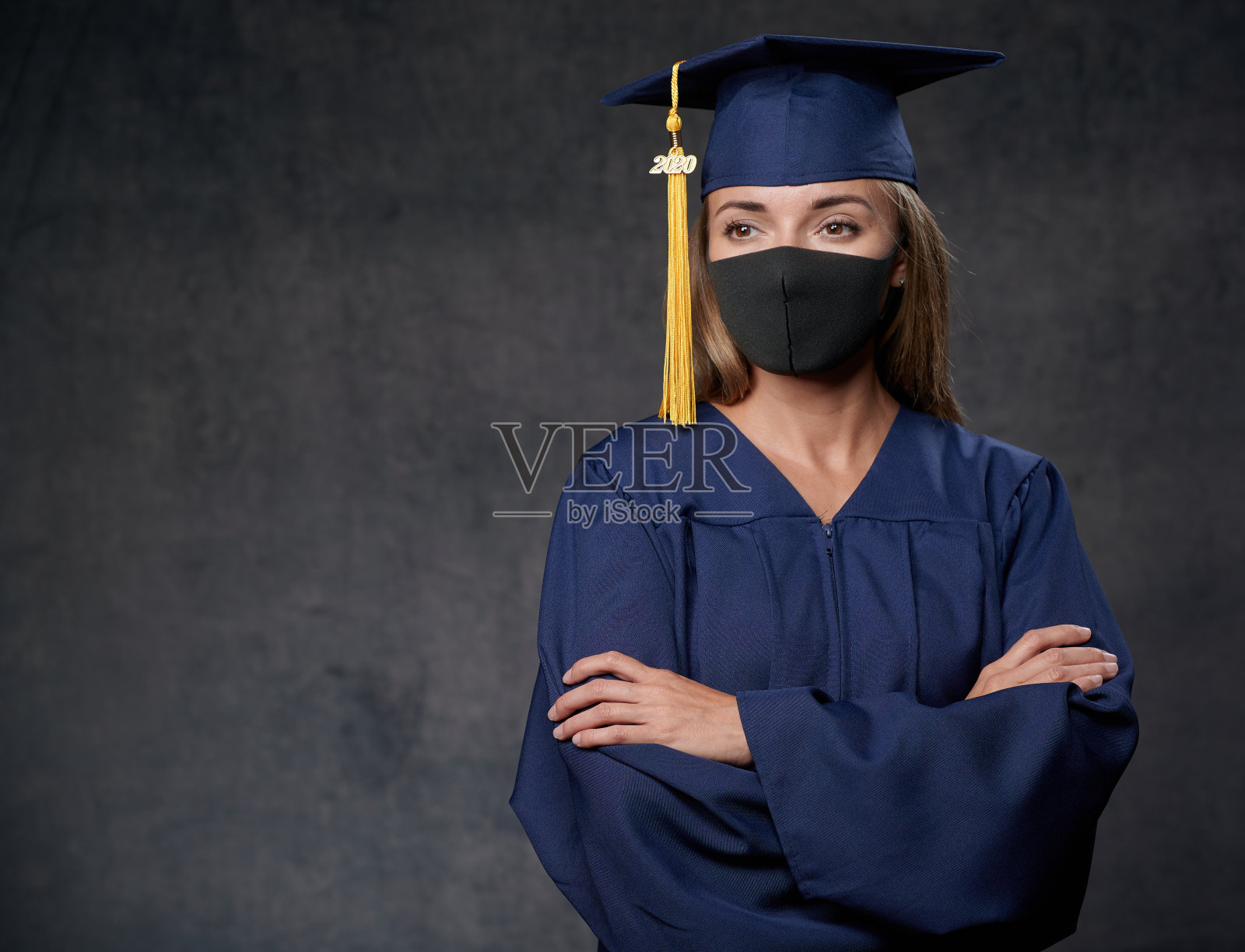 年轻的女毕业生双手放在一边,戴着蓝色的帽子和长袍,还戴着黑色的面具庆祝她的大学学位照片摄影图片