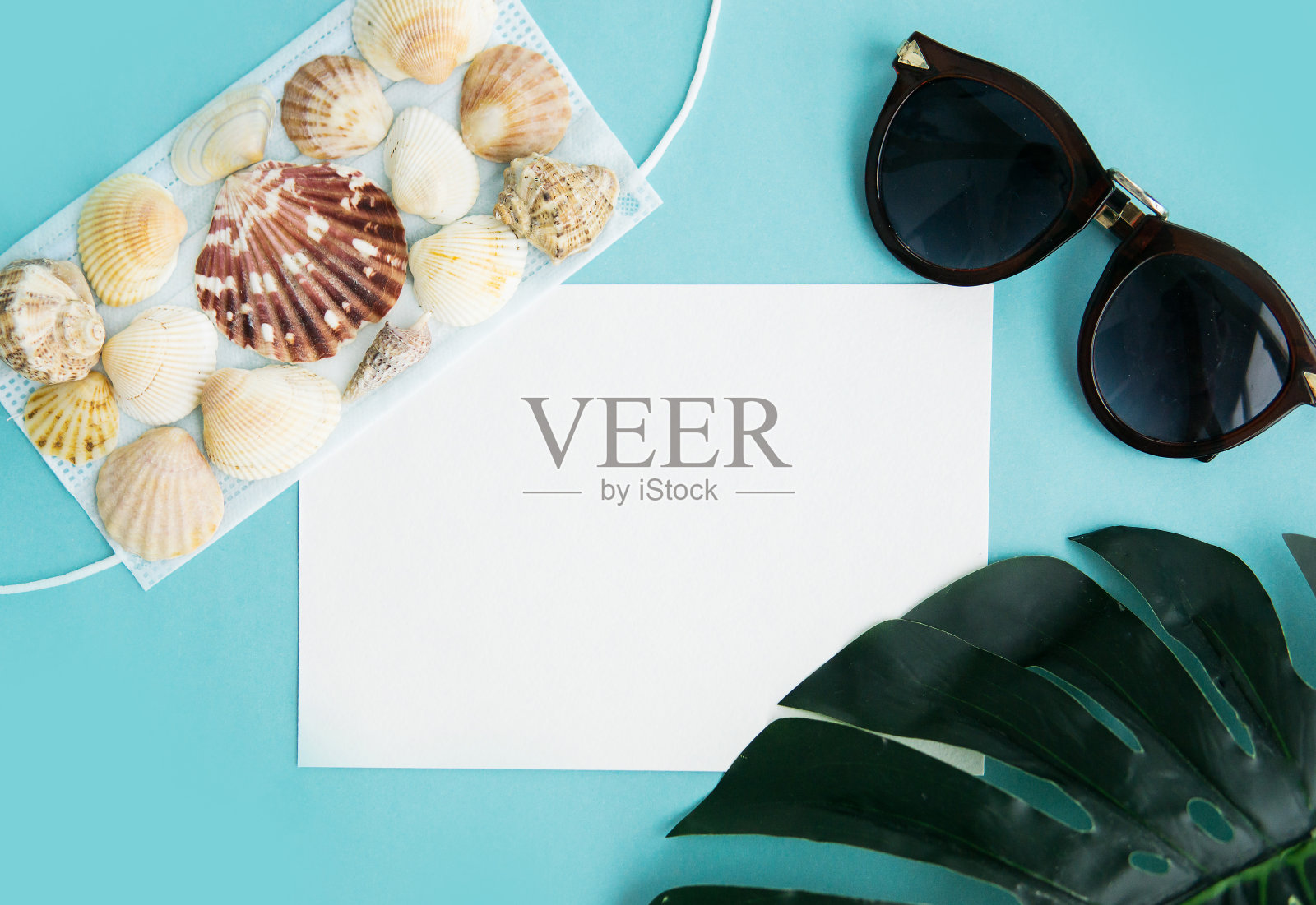 医用口罩、太阳镜和蓝色背景的贝壳。平铺、复印空间、度假取消、流行、旅游。照片摄影图片