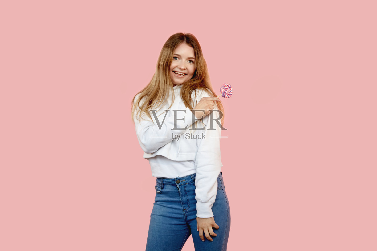 穿着牛仔裤拿着棒棒糖的有趣女孩微笑着看着镜头照片摄影图片