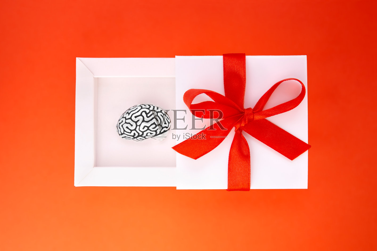 这个有趣的礼物是一个装在白色礼品盒里的小钢铁人脑复制品,盒子的封面上有红色的丝带和蝴蝶结。照片摄影图片