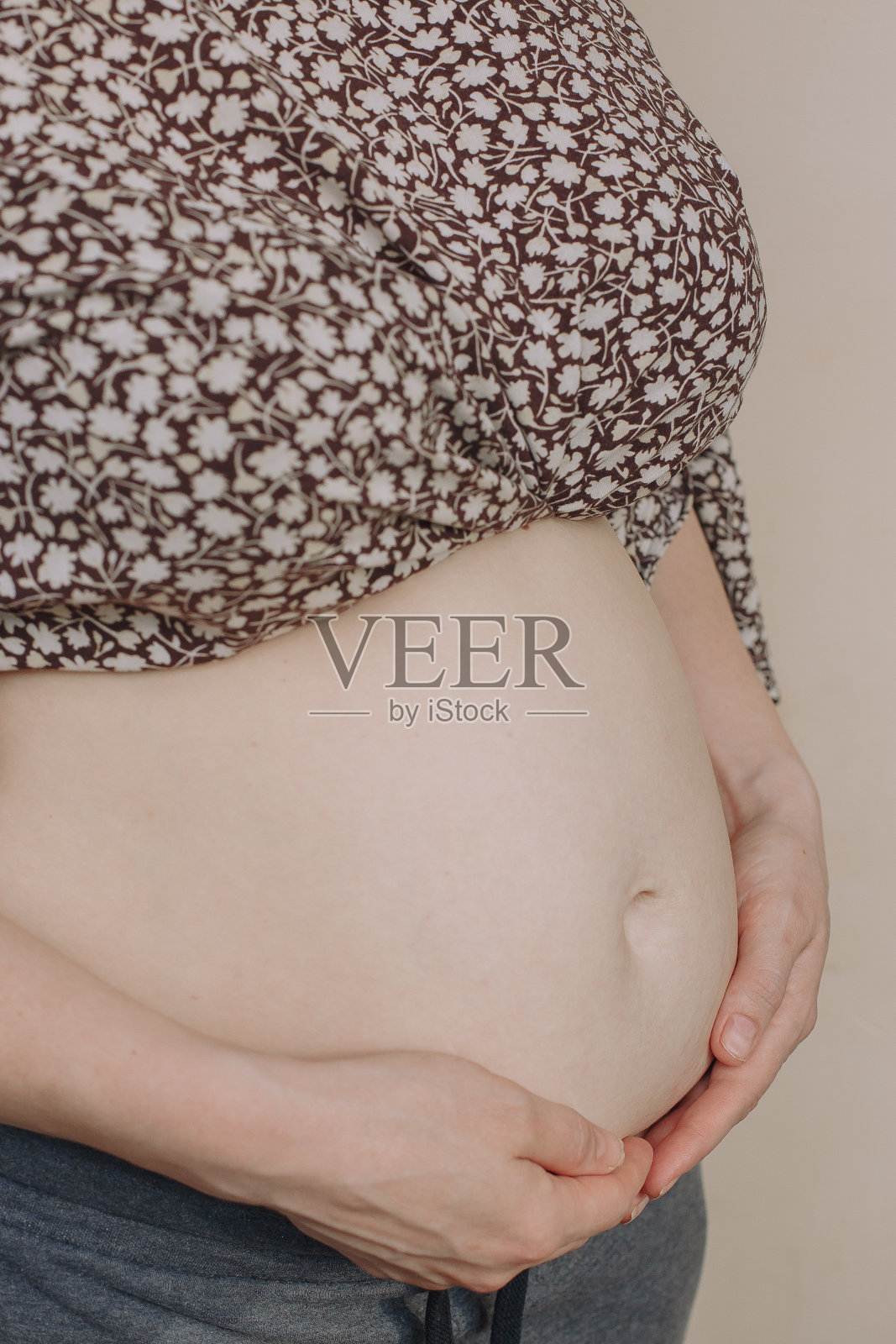 一个孕妇的肚子的特写。一个怀孕的女孩站在米色的背景上,用手捂着肚子照片摄影图片