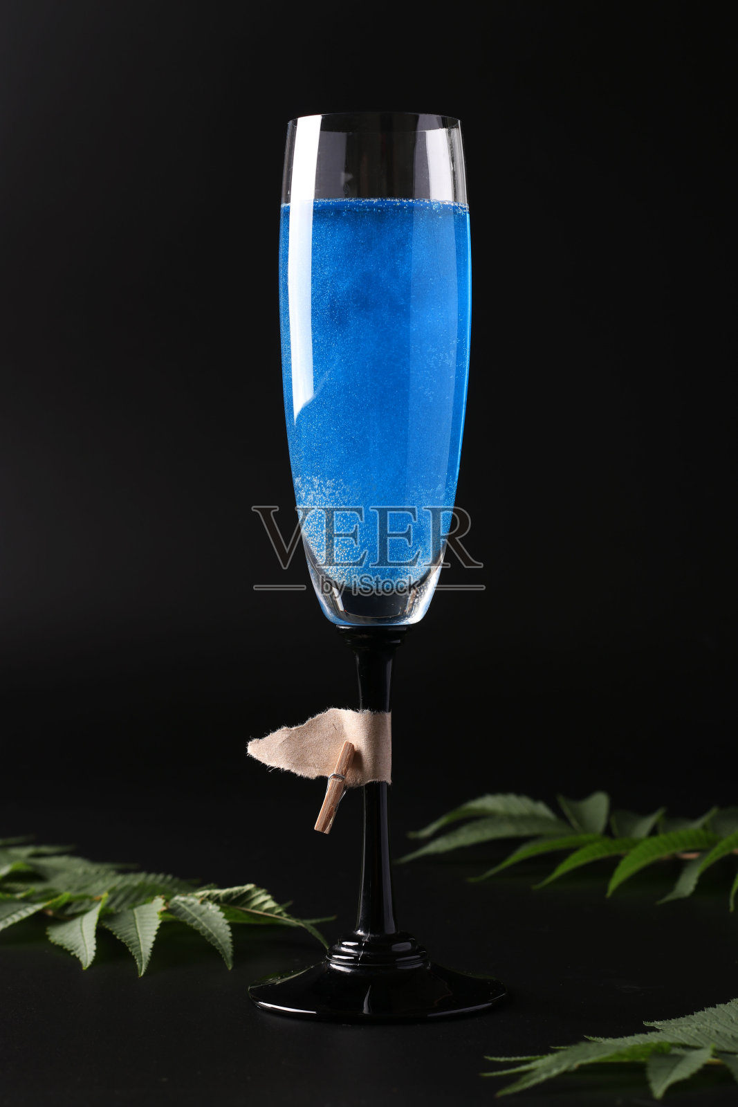在黑色的背景下,高脚杯中闪烁的蓝色气泡酒。垂直格式。特写镜头照片摄影图片