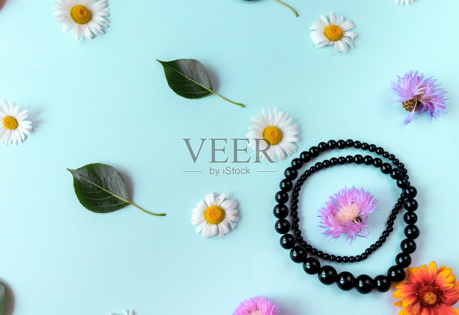 在蓝色的背景上有鲜花、珠宝和绿叶。平的。照片摄影图片