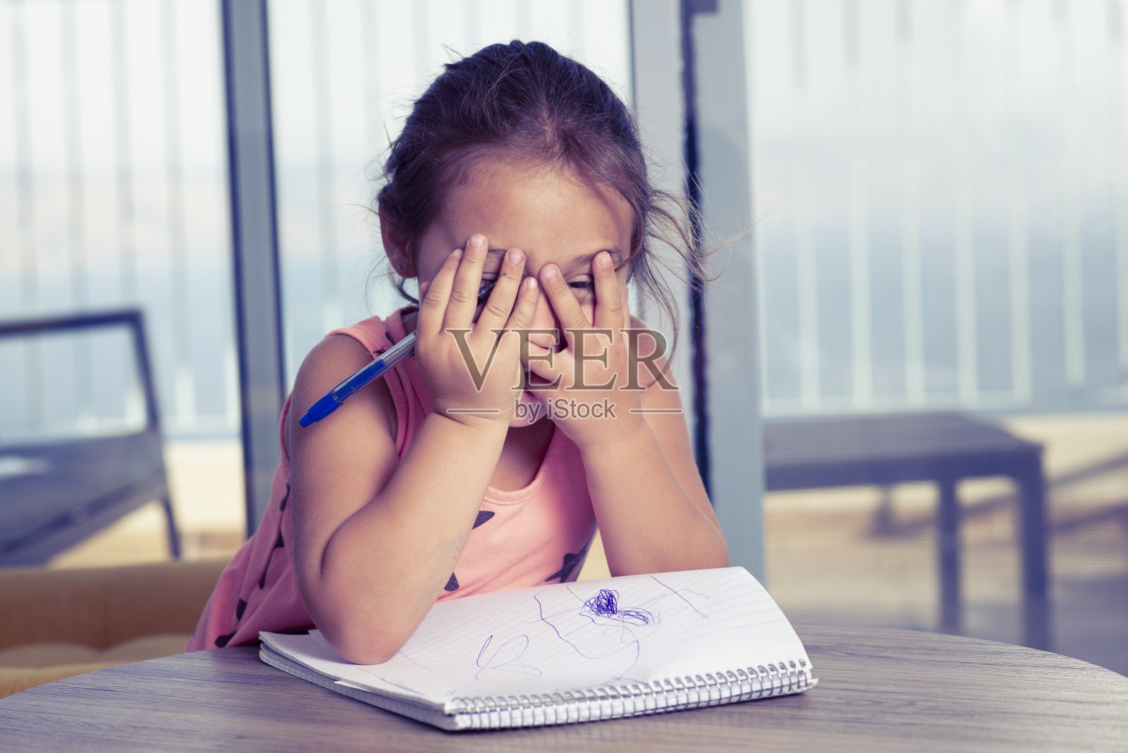 害羞的女孩用手遮住脸。写作启蒙阶段。儿童在家进行写作能力培养。照片摄影图片