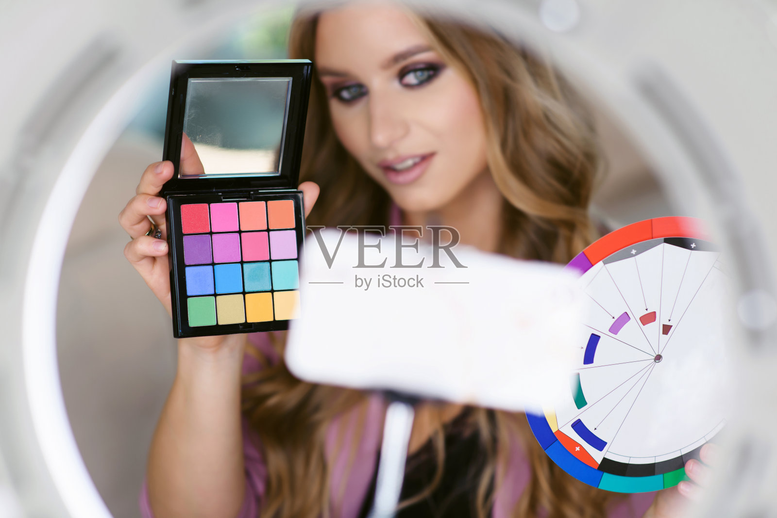 年轻迷人的女子博客流关于化妆。这位著名的化妆师正在谈论她的新阴影调色板,并使用智能手机和环形灯来录制她的在线美容课程照片摄影图片