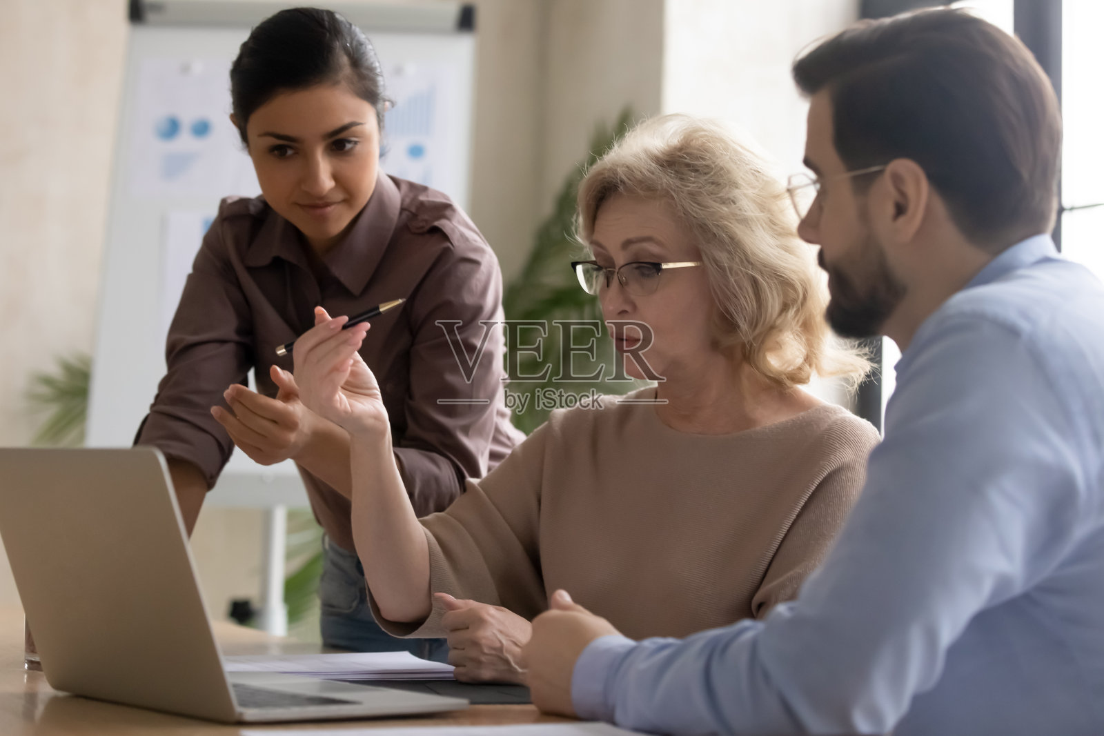 严肃成熟的女商人使用笔记本电脑与不同的经理签订合同。照片摄影图片