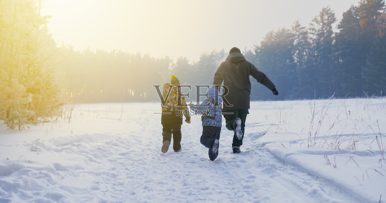 幸福的家庭:母亲,父亲和两个孩子在雪地上奔跑,在冬天的夕阳下照片摄影图片