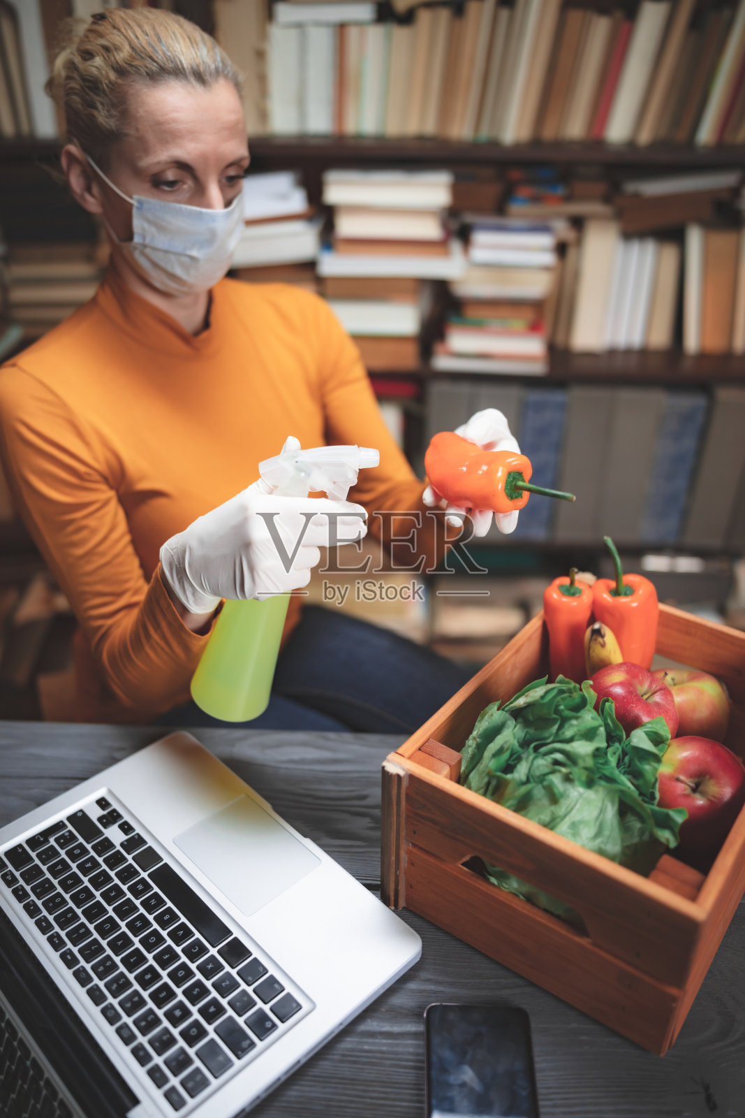 戴着医用防护口罩的妇女在网上订购的食品上喷洒消毒液。照片摄影图片
