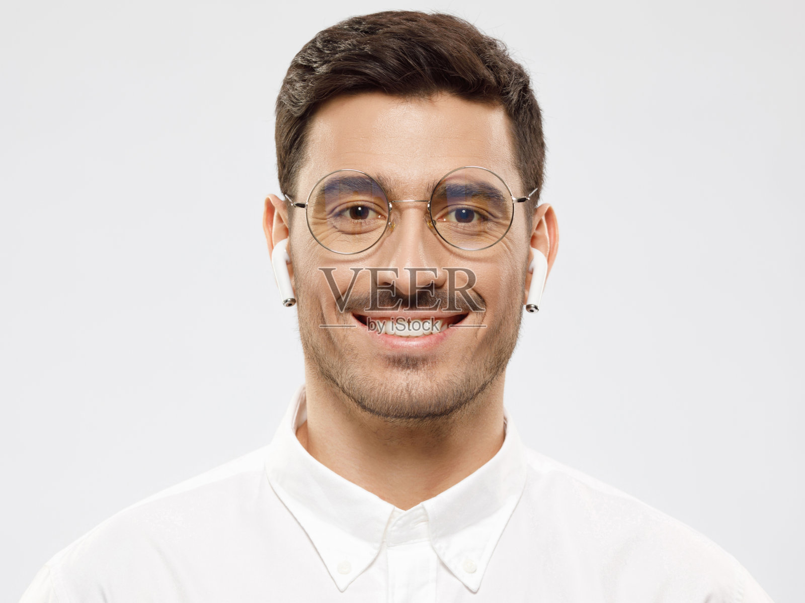 特写的现代年轻商人穿着白色衬衫,无线耳机和圆眼镜,孤立在灰色背景照片摄影图片