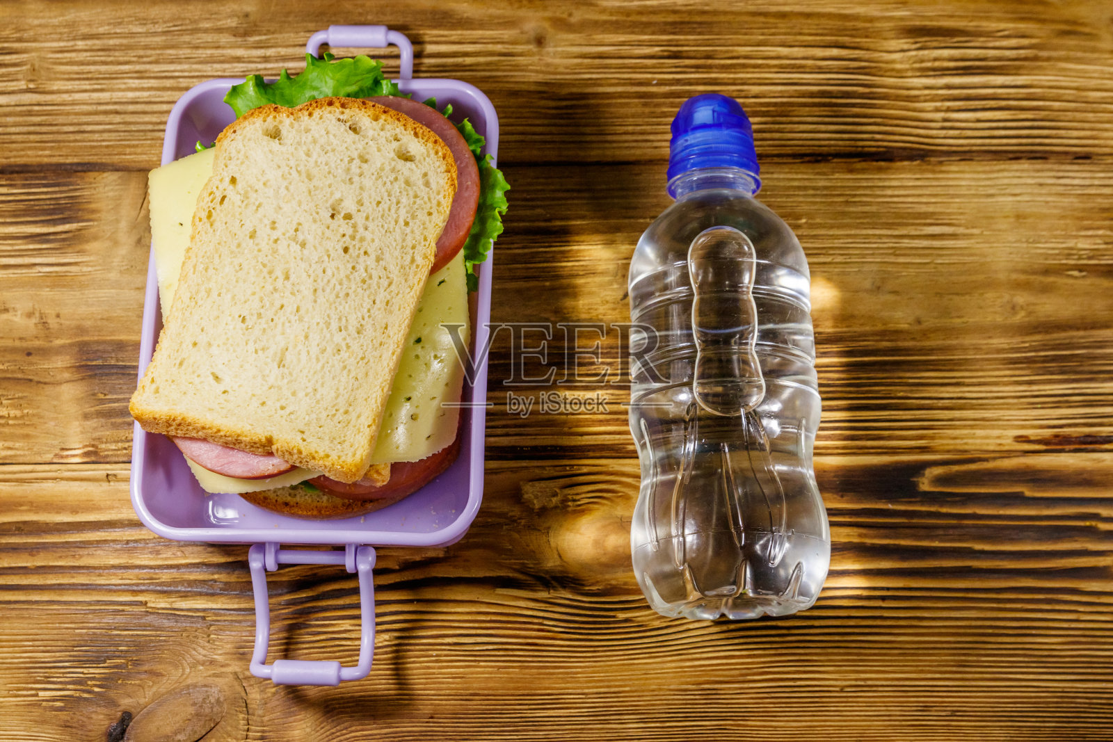 木桌上放着午餐盒,里面有三明治和一瓶水。俯视图照片摄影图片