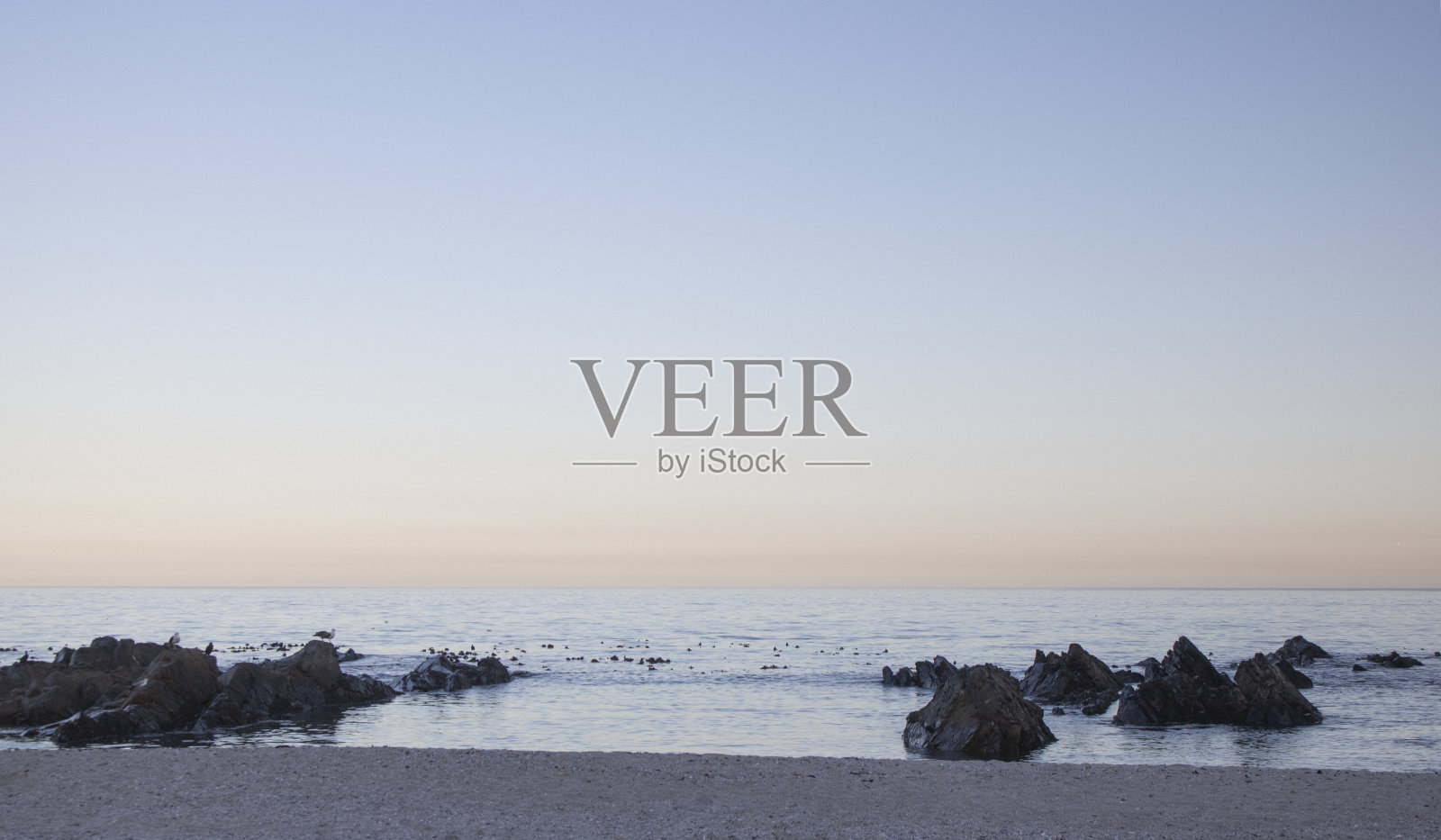 日出或黎明时分,海滩上有岩石和平静的海水。照片摄影图片