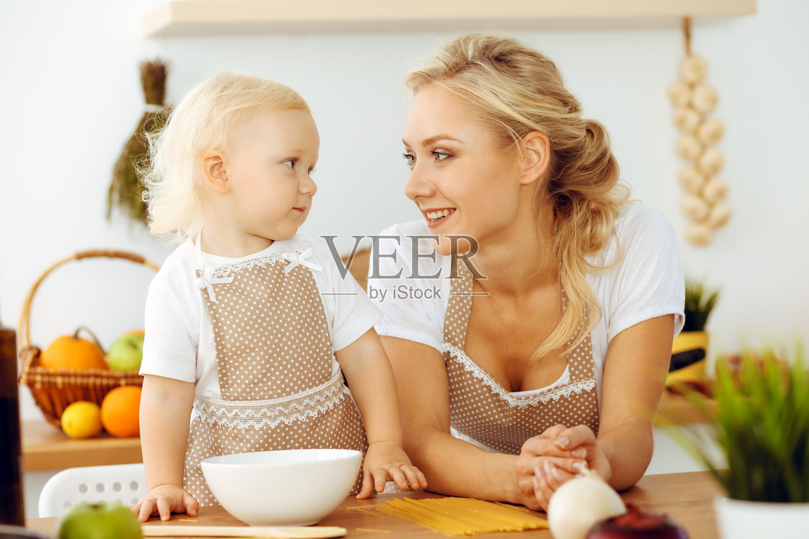 快乐的妈妈和小女儿在厨房做饭。花时间在一起,家庭乐趣的概念照片摄影图片