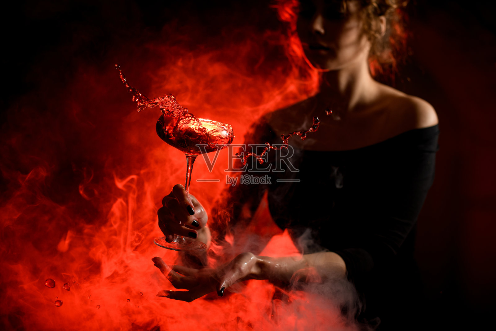 年轻漂亮的女人拿着玻璃杯,在她面前泼洒着明亮的鸡尾酒。照片摄影图片