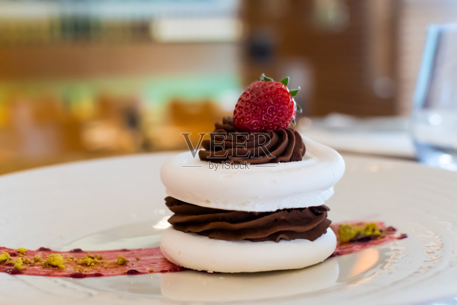 蛋白蛋糕上面有黑巧克力和草莓,在餐厅背景下,模糊的背景照片摄影图片