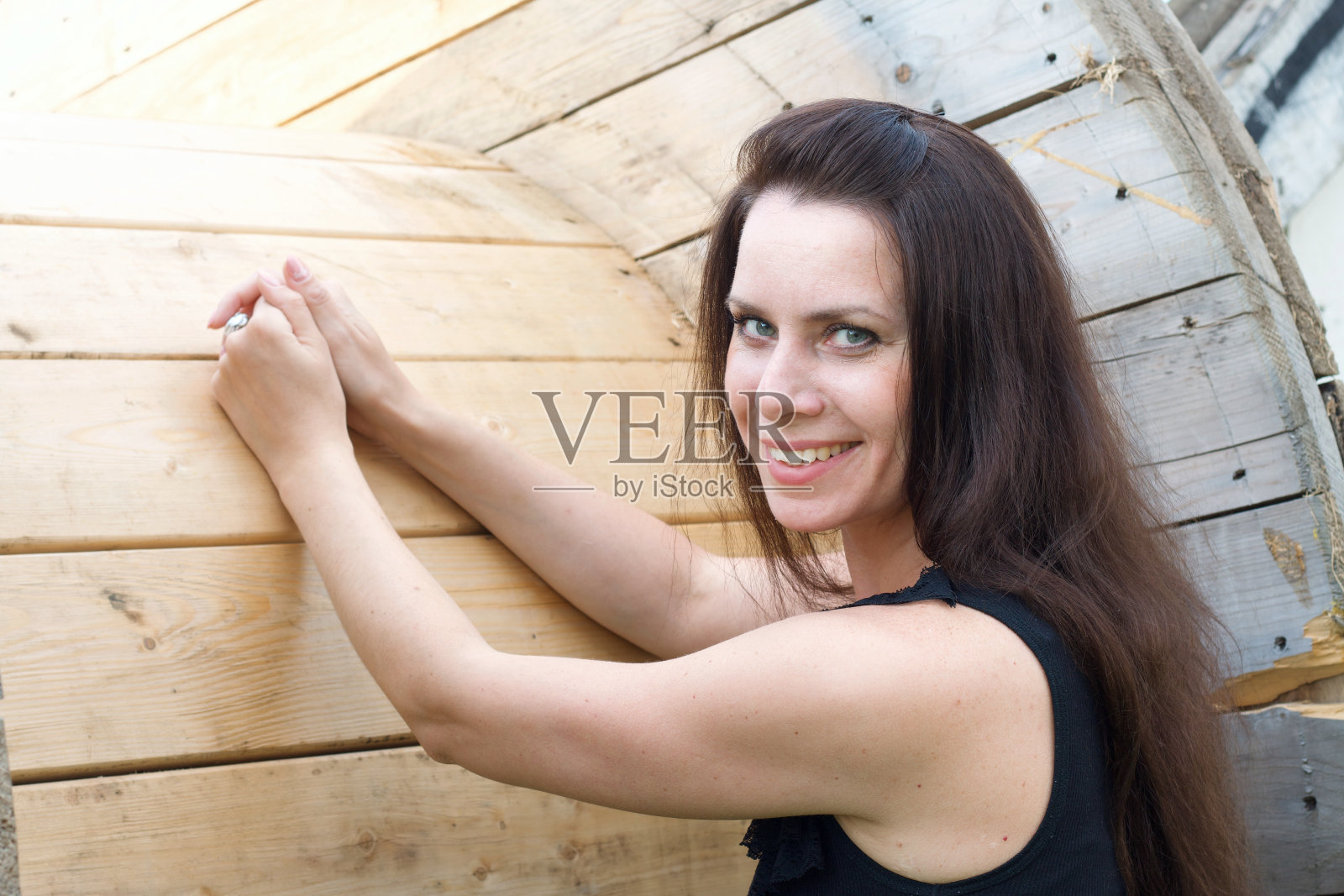 女孩在一个木制电缆卷轴附近摆姿势。把你的手放在卷轴上。照片摄影图片