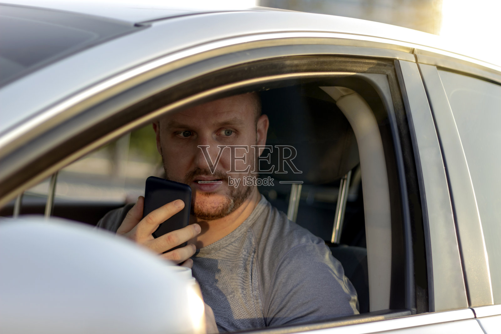 微笑的男人坐在车里,用手机。照片摄影图片