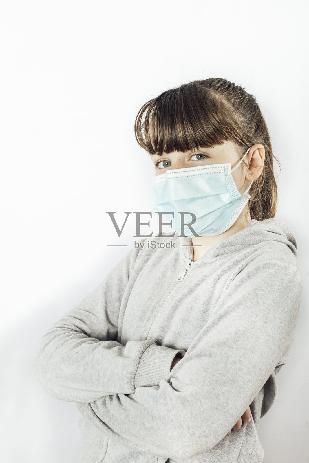 年轻女孩看着镜头,双手交叉戴着医用口罩。白色背景照片摄影图片