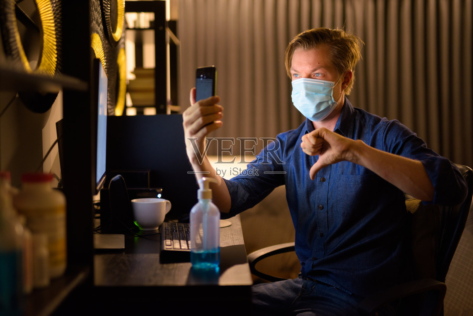 年轻的商人戴着面具,在深夜在家工作时,不停地给人打视频电话照片摄影图片