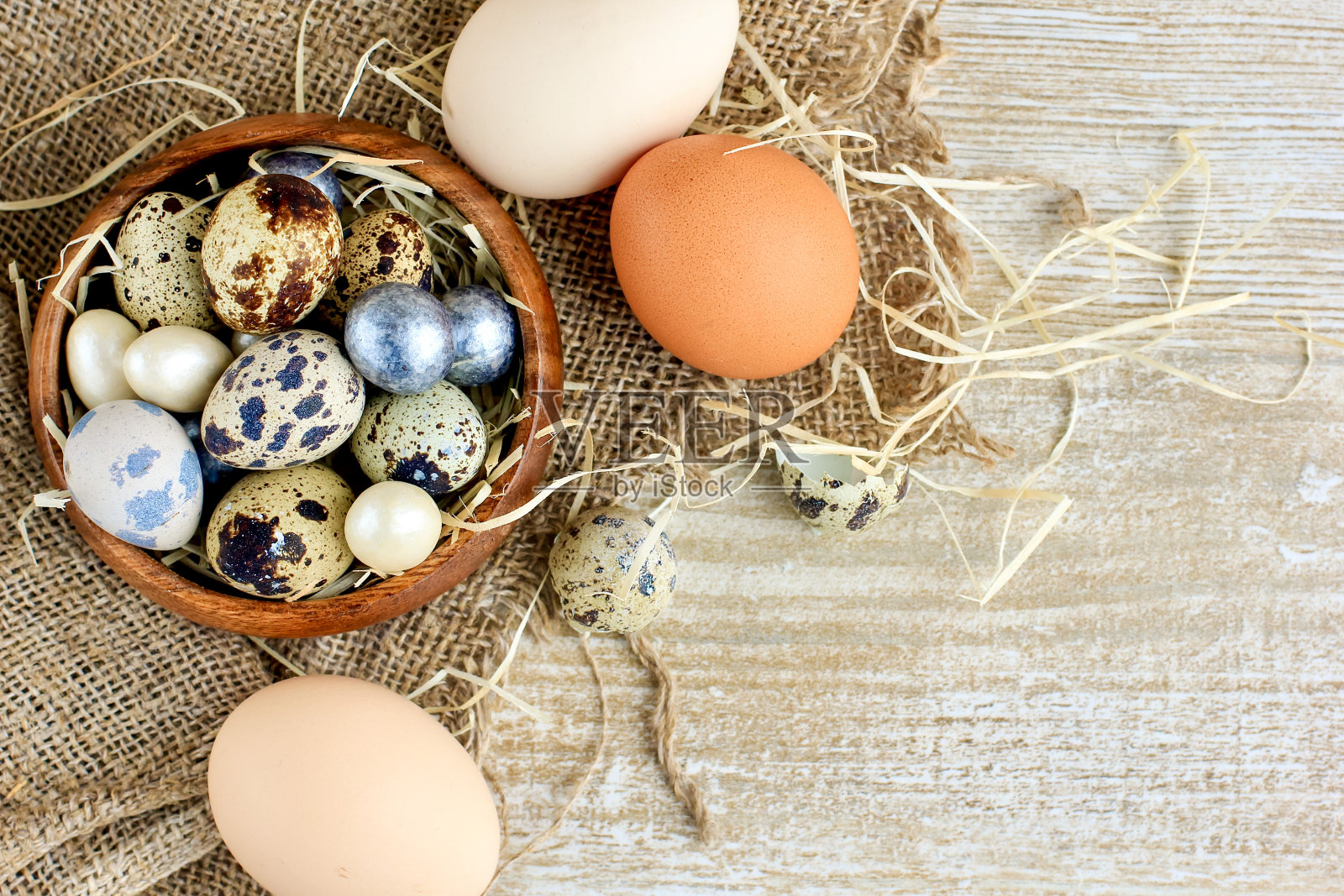 颜色斑驳的鹌鹑蛋,银色和白色的糖果躺在一个木碗上的粗麻布在乡村的背景。复活节和食物的概念。照片摄影图片