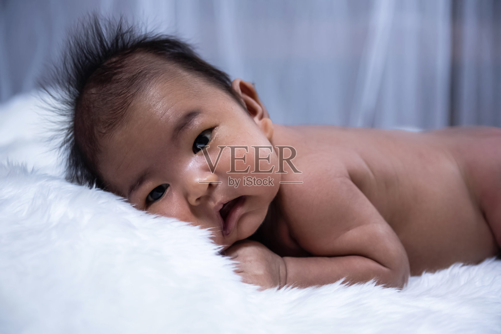 刚出生的婴儿躺在丝绒布上,饶有兴趣地看着什么东西,四周模糊的光线照片摄影图片