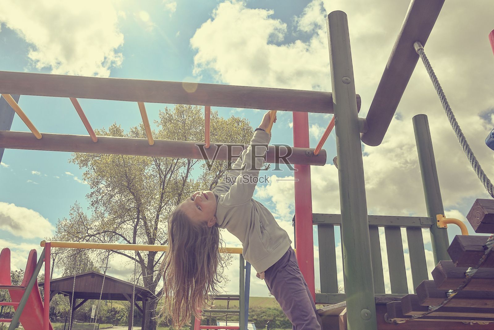 小女孩在操场上玩耍,吊着走在猴架上。照片摄影图片