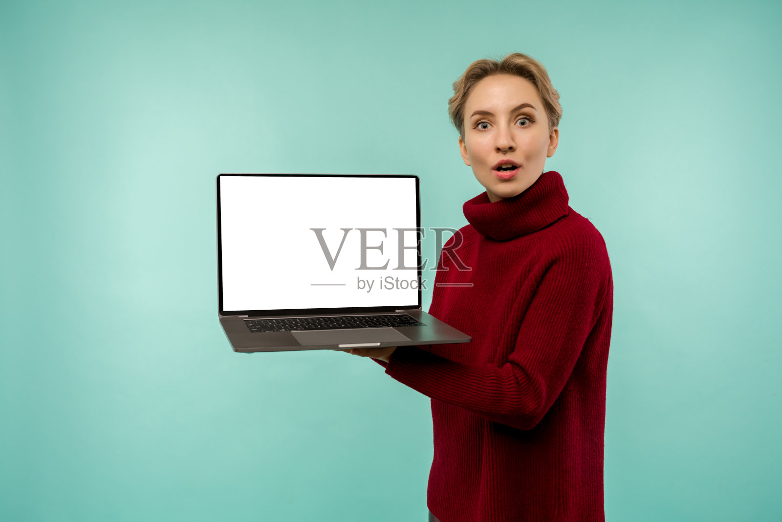 身着红色毛衣的女孩展示了一个蓝色背景下的空白笔记本电脑屏幕照片摄影图片