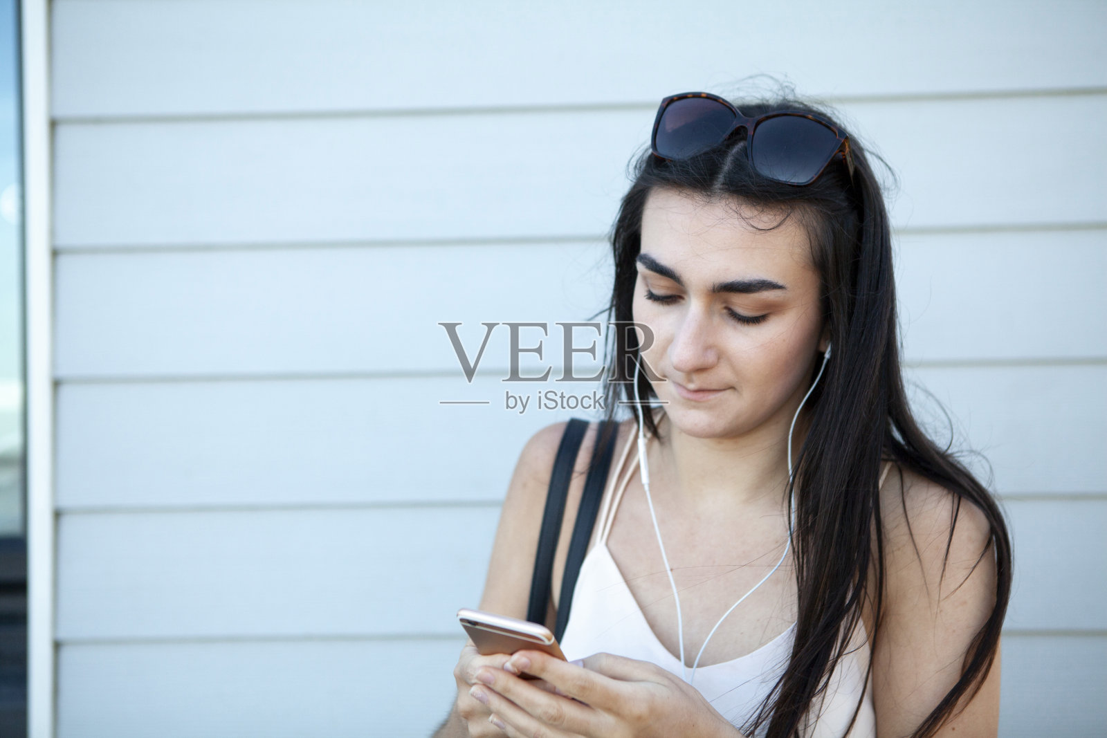 夏天,一个十几岁的女孩在浅蓝色的沙滩木屋边用手机发短信照片摄影图片