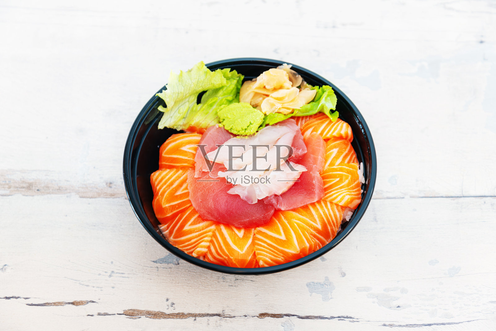 日式Chirashi由三种生鱼片,鲑鱼,金枪鱼和鳕鱼搭配制成,配以芥末酱和姜片放在碗里的白醋饭。照片摄影图片